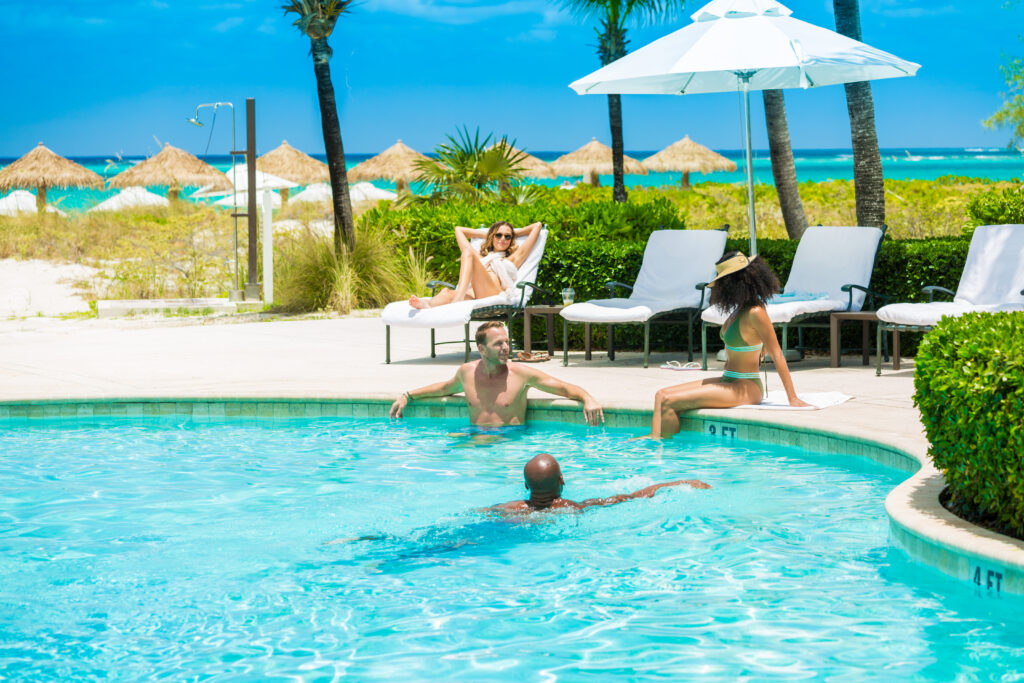 Three people in the pool and one person on a lounge chair.