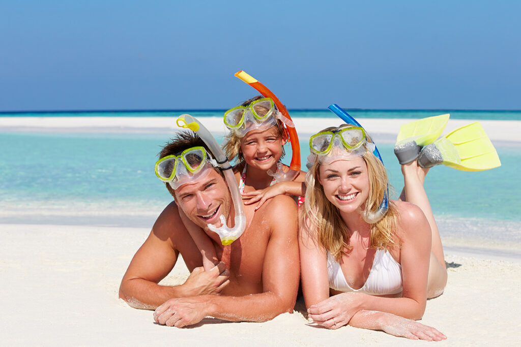 Parents and little girl smiling on the beach in snorkeling gear